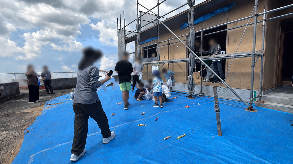 外で餅やお菓子を拾っている写真 新築住宅の上棟式で餅投げを楽しむご家族の様子